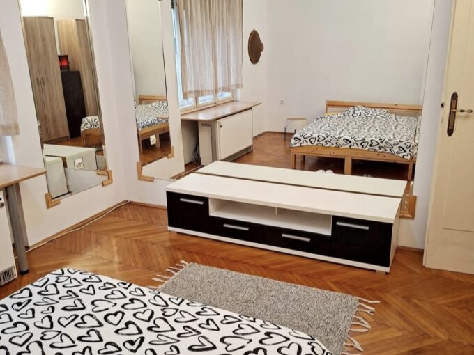 Bedroom with a bed in the foreground covered by a white duvet with black heart patterns, plus large wall mirrors and wooden furniture.